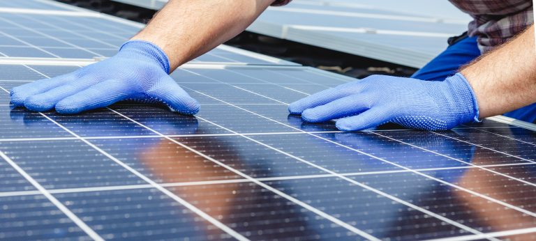 Male worker hands in glows on solar panel, technician installing solar panels on roof. Alternative energy sun energy power, ecological concept